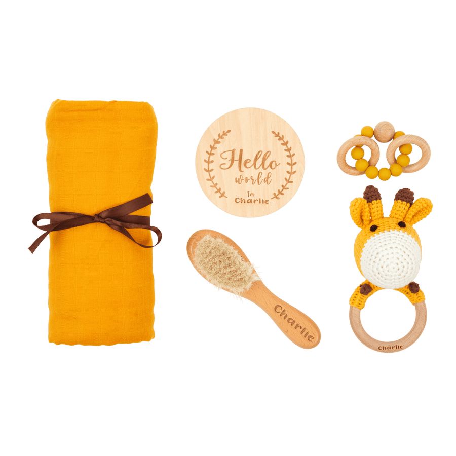 A newborn gift set including a yellow blanket, a giraffe-shaped rattle, a wooden brush, and a 'Hello, world' keepsake plaque with a giraffe design.