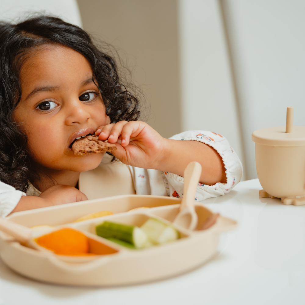 Child eating from a divided plate with food on a white surface
