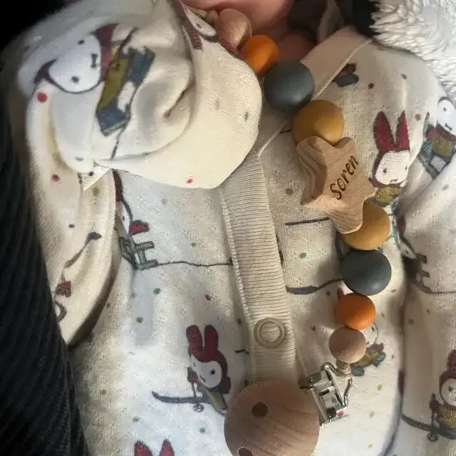 Close-up of a baby's outfit with a personalised star dummy clip in orange