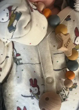 Close-up of a baby's outfit with a personalised star dummy clip in orange