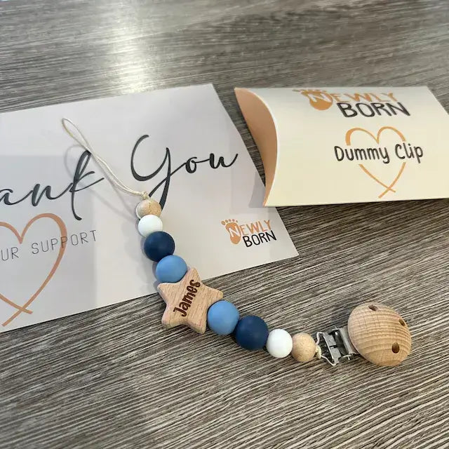 Personalised dummy clip with wooden and silicone beads on a wooden surface with Newly Born Packaging