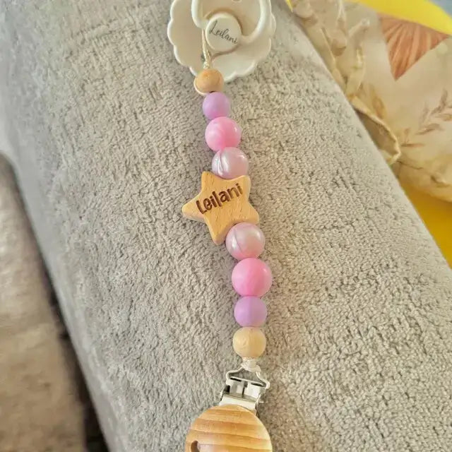 Personalised Pink star dummy clip with colorful beads and a star-shaped name tag on a textured surface.