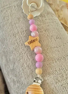 Personalised Pink star dummy clip with colorful beads and a star-shaped name tag on a textured surface.
