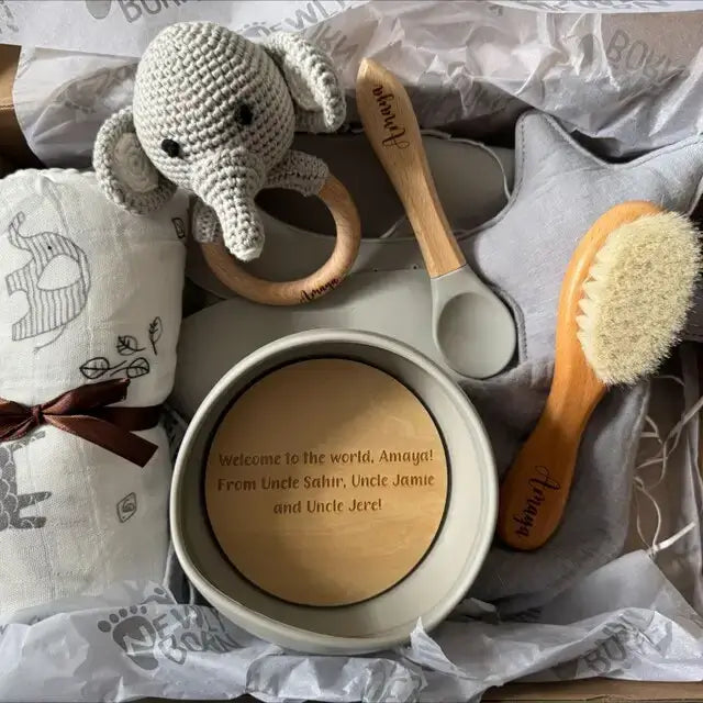 Personalised baby shower gift items including a teether, brush, and personalized bowl with a baby blanket and elephant toy.