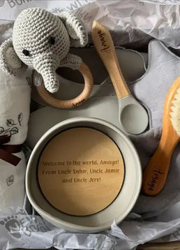 Personalised baby shower gift items including a teether, brush, and personalized bowl with a baby blanket and elephant toy.
