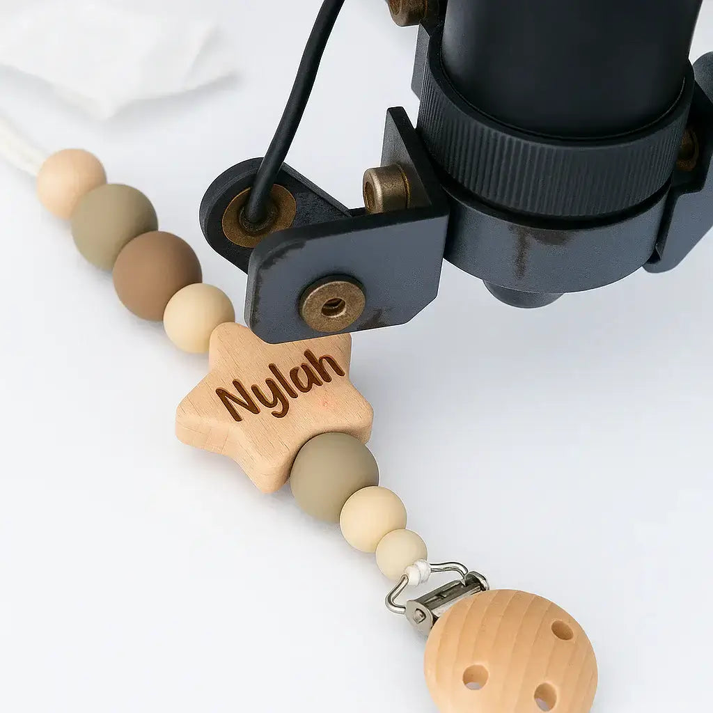 Wooden laser engraving pacifier clip with star-shaped name tag and beige beads on a white background